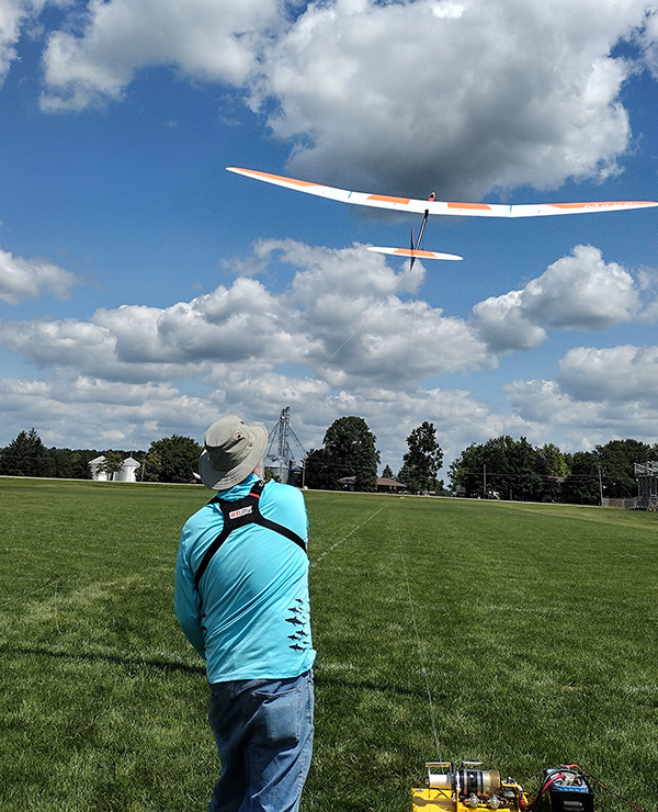 Man flying a remote-controlled glider in a grassy field.