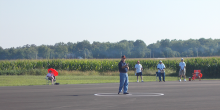 Man standing on tarmac with trees and fields in the background.